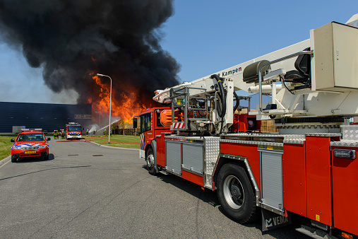 Kampen, The Netherlands - June 8, 2013: Fire fighters trying to put out a fire in an industrial area in the town of Kampen in The Netherlands. Trucks are parked on the road while firefighters in the distance are trying to put out the fire.