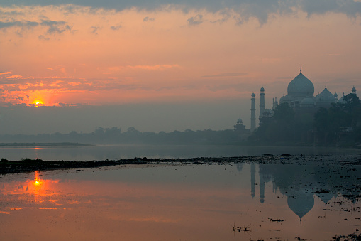 Word famous Taj Mahal in Agra, India - seen from an usual standpoint at the banks of Yamua River. Early morning on a misty day, with reflections in the River. 