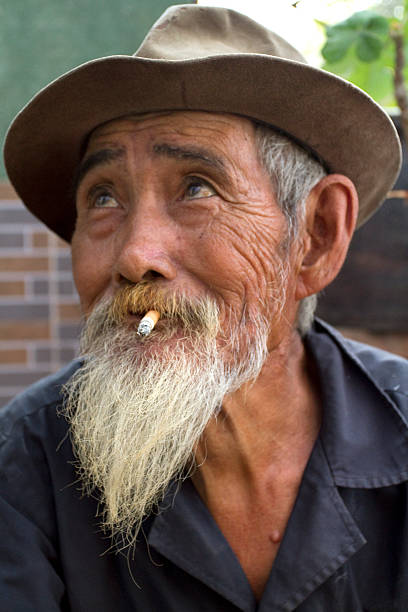 Local people Hanoi, Vietnam - 04 April 2013: There is a man on this photo. He is sitting on the street and smoking a cigarette. vietnamese old man portrait stock pictures, royalty-free photos & images