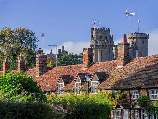 cottage Warwick, UK - November 4, 2012: Warwick castle, one of the main tourist attractions in the English Midlands can be seem behind a row of old cottages, in the centre of the county town of Warwickshire. It is a sunny afternoon in Autumn.  warwick uk stock pictures, royalty-free photos & images