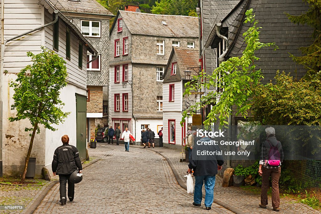 Small street of Monschau Monschau, Germany - May 31, 2013: Monschau lies in a narrow and deep valley in the Eifel along a river. The historic architecture and abundant greenery give Monschau its unique character. The town has a large amount of half-timbered houses, quaint shops and cozy cafes. In the photo is a narrow street with cobblestones to see and people to visit the town of Monschau. Aachen Stock Photo