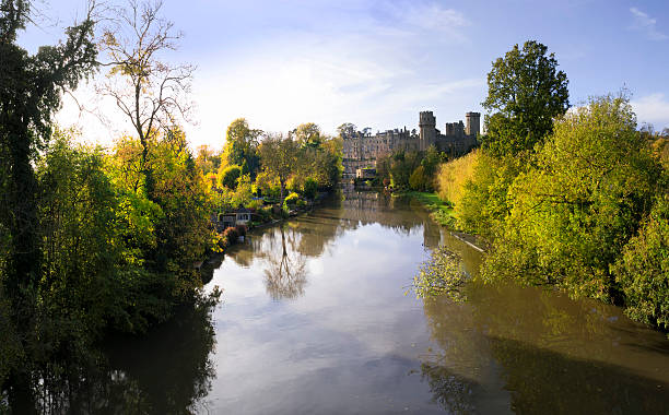 warwick castle Warwick, UK - November 4, 2012: This is Warwick castle viewed across the River Avon, Warwick is the county town of Warwickshire and is also a popular tourist destination in the English Midlands, England UK. The Castle is also popular with visitors. This is a sunny afternoon in Autumn and the trees alongside the river are very colourful. warwick uk stock pictures, royalty-free photos & images