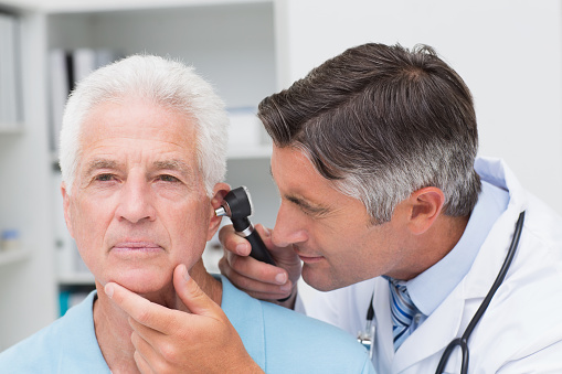 Male doctor examining senior patients ear with otoscope in clinic