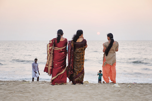 Kozhikode, Kerala,India - January 16 , 2013: Three women in  traditional dress  standing near the sea on the Calicut beach. They are watching the sunset.  Kozhikode, formerly known as Calicut, is a city on the Malabar coast in southern India.