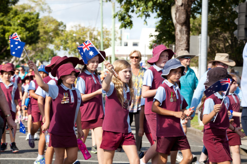 Mackay, Australia – April 25th, 2013: School children in uniform waving Australian flags and wearing war medals, marching in a memorial ANZAC Day annual march.