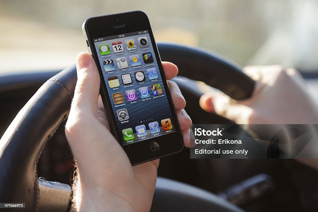 Man using iPhone 5 in car Nizhnevartovsk, Russia - June 12, 2013: Man hand holding iPhone 5 in the car. App on desktop Messages, Calendar, Photos, Camera, Video, Maps, Weather, Passbook Notes, Reminders, Clock, Stocks, Newsstand, iTunes, App Store, Settings, Phone, Mail, Safari, Music. iPhone is product Apple Inc. Adult Stock Photo