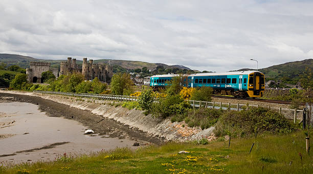 Arriva Trains Wales Train diesel Unit Passes Conwy Castle Conwy, Wales - June 2, 2013: Arriva Trains Wales Train diesel Unit Passes Conwy Castle: Conwy Castle and a Arriva Trains Wales Train travelling through the welsh countryside. The railway embankment meets the sea and is covered with trees and shrubs but you can still see the Arriva Trains Wales Train as it passes the medieval castle at Conwy on the North Wales coast. with the raised embankment the train is above the shore line of the sea. conwy castle stock pictures, royalty-free photos & images