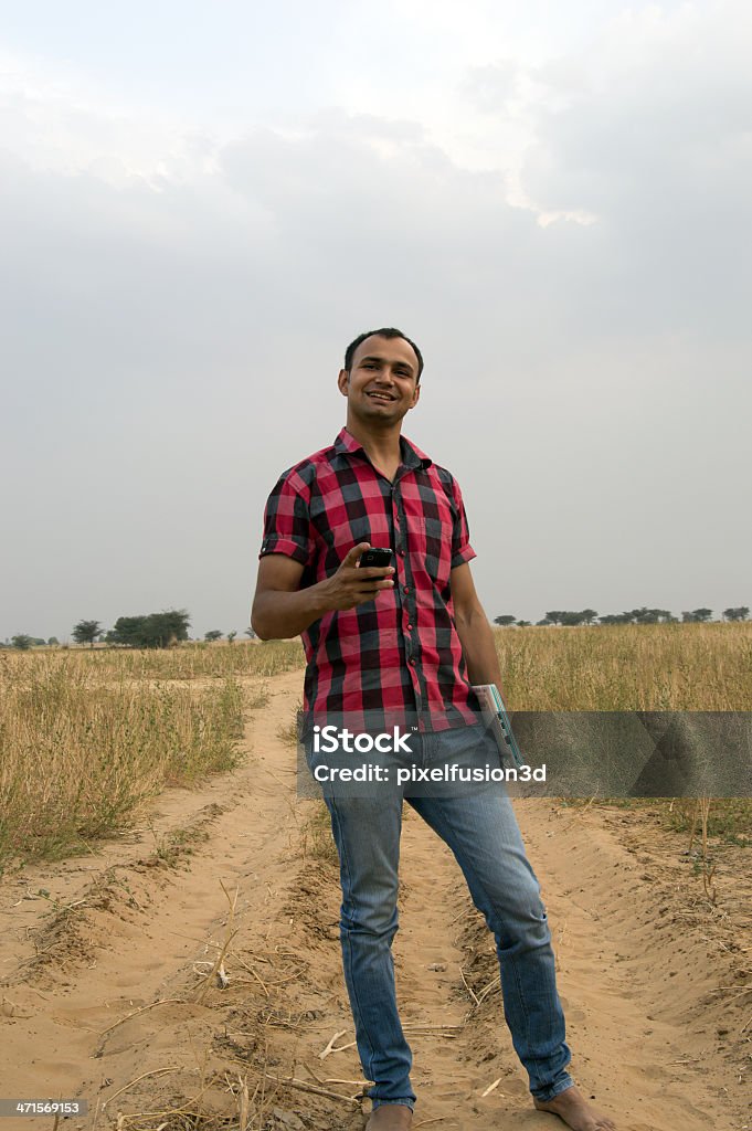 Man Standing in The Field Holding Laptop Cheerful Indian Man Standing in the Field Holding Laptop and Smart Phone. Activity Stock Photo