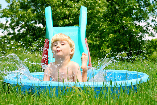 A young child slides into a small swimming pool and makes a splash, on a sunny summer day