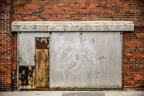 Old metal shop door on brick wall An old weathered door on a brick wall. graffiti brick wall dirty wall stock pictures, royalty-free photos & images