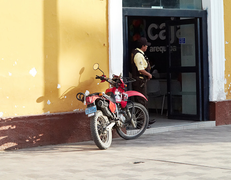 Ica, Peru - May 20, 2013: Security guard standing in doorway of bank in the Peruvian city of Ica. A red motorcycle is parked against the yellow coloured wall