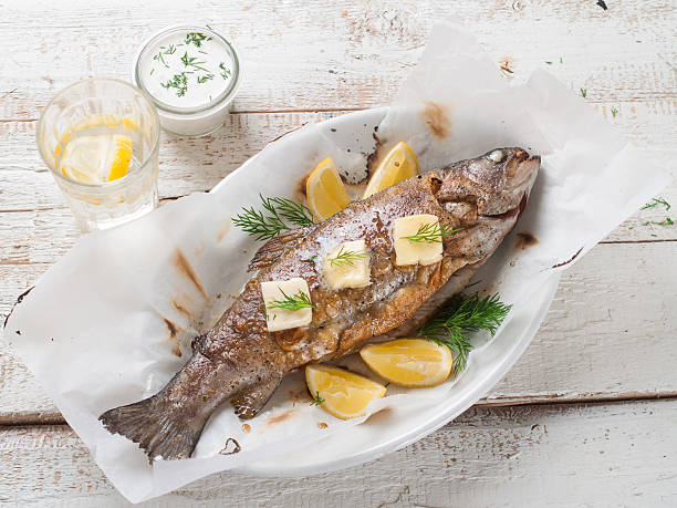 Top-down shot of whole grilled fish with lemon slices Grilled fish with butter and lemon, selective focus trout stock pictures, royalty-free photos & images