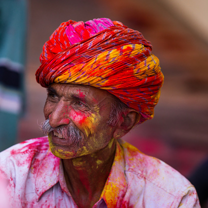 Indian senior man wearing a turban with face covered in color powder