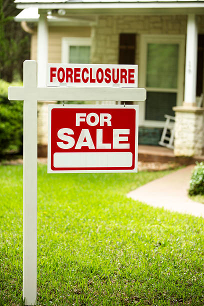 Foreclosure, house for sale sign. Front yard of home. Nobody. Red and white "Foreclosure, Home for Sale" sign in front of a stone, wood house that is for sale and is being foreclosed upon by a financial institution. Green grass and bushes indicate the spring or summer season. Front porch and windows in background.  Economic depression, recession, bankruptcy concepts. foreclosure stock pictures, royalty-free photos & images