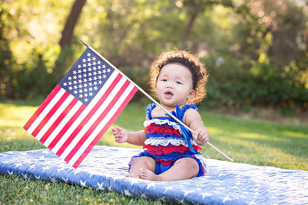 Patriotic Baby Girl Waving American Flag Beautiful six month old multi ethnic baby girl sitting on a blanket and waving an American Flag. 4th of July. patriotic quilt stock pictures, royalty-free photos & images