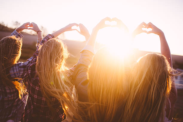 Rearview of a row of teens using their hands to make heart shapes at sunset