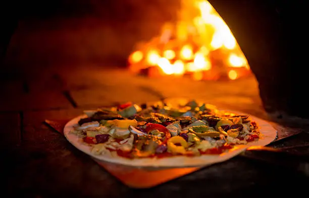 Delicious freshly made vegetarian pizza carefully being carried to a traditional wood fire oven