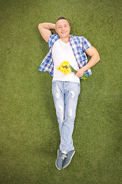 istock Young guy lying on grass and holding flowers 471577240