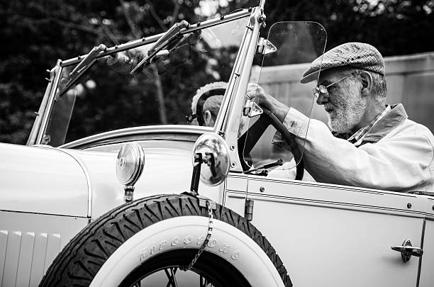 Bedford, Nova Scotia, Canada - June 18, 2013: A man driving a replica of a 1929 Ford Model A Roadster which was sold between 1979 and 1986.  A passenger is visible as well.  TOned black and white.  Car is part of a public gathering of automobiles at the Chickenburger restaurant in Bedford, Nova Scotia.
