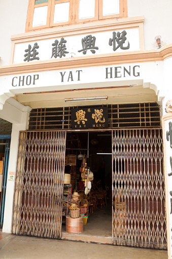 Melaka, Malaysia - September, 18th 2012: Old shop in old colonial building in Chinatown of Melaka. Name of shop is Yat Heng. Entrance has old grid iron sliding and foldable door. Inside are cages and chairs.