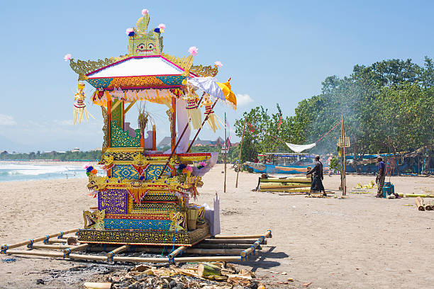 Ornate Funeral Casket on Kuta Beach, Bali Kuta, Indonesia - September 25, 2014: An ornate funeral casket used for transporting the body of the deceased to the cremation site, sits on the beach at Kuta, Bali, while the body is cremated in the background. kuta beach stock pictures, royalty-free photos & images