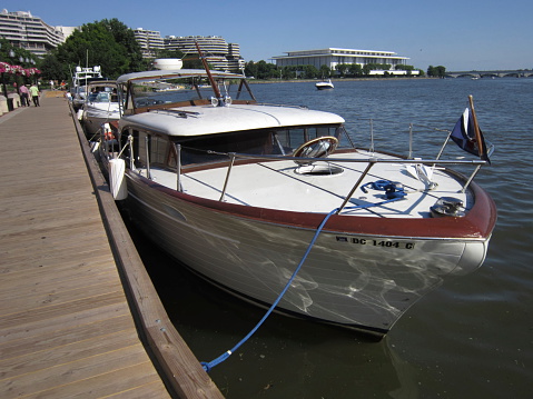 Washington DC, USA - June 21, 2013: A vintage Chris Craft boat is docked at the Georgetown Waterfront in Georgetown of Washington DC.  The Kennedy Center and Watergate are in the background.
