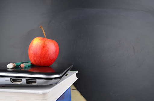 A stack of books with an apple and blackboard with text written in white chalk.