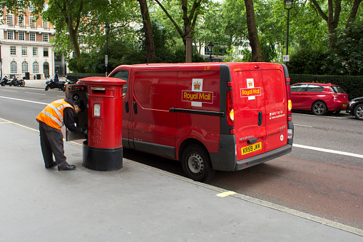 London, UK - June 22, 2013: Royal Mail man collecting the mail from a post box in London. Here you can see his vehicle next to the post box, so that he can easily collect the mail and put it in his vehicle for efficiency. Royal Mail is one of the primary methods for delivering items such as letters and parcels in the UK.