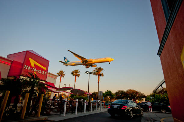 Los Angeles, USA - May 13, 2013: Airplane flying over In-n-Out Burger, LAX, few cars are leaving In-n-out parking lot. People eating outside the restaurant.