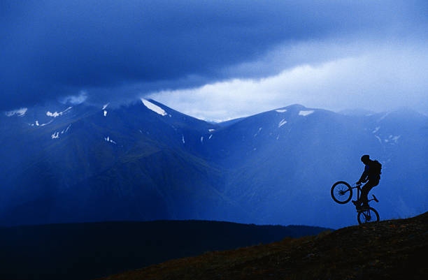 A male mountain bike rider pops a wheelie during a rainstorm near the city of Whitehorse, Yukon, Canada. 