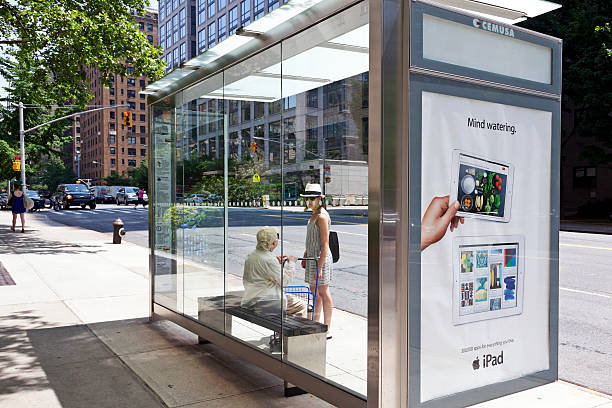 New York City New York City, USA - June 22, 2013: A young woman is talking with an elderly woman sitting in a bus shelter with advertising of the apps for the iPad on West End Avenue. bus shelter stock pictures, royalty-free photos & images