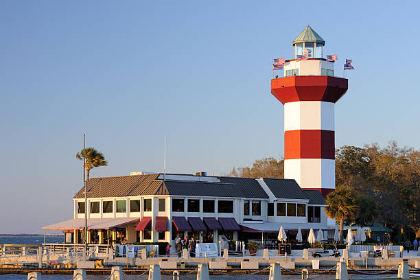 Harbor Town Hilton Head Island, USA - March 25, 2013. Hilton Head lighthouse with people out or inside the restaurant. Hilton Head Island or Hilton Head is a resort town named after Captain William Hilton who found this headland in 1663. It is a population vacation destination in South Carolina, with a 12-mile long beach on Atlantic Ocean. hilton head photos stock pictures, royalty-free photos & images