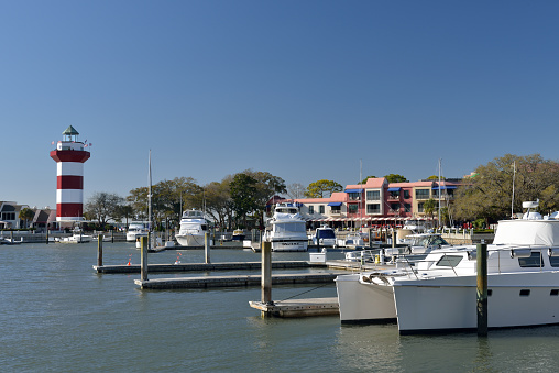 Hilton Head Island, USA - March 25, 2013. Yacht basin view with people on lighthouse or sitting outside restaurants or walking around in background. Hilton Head Island or Hilton Head is a resort town named after Captain William Hilton who found this headland in 1663. It is a population vacation destination in South Carolina, with a 12-mile long beach on Atlantic Ocean.
