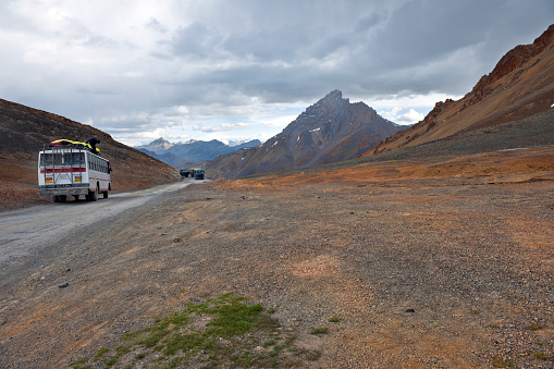 Lachulung La, Jammu and Kashmir, India - July 23th, 2011: Man on local bus arranging the baggage, three military vehicles driving, on Leh-Manali highway, Northern India.