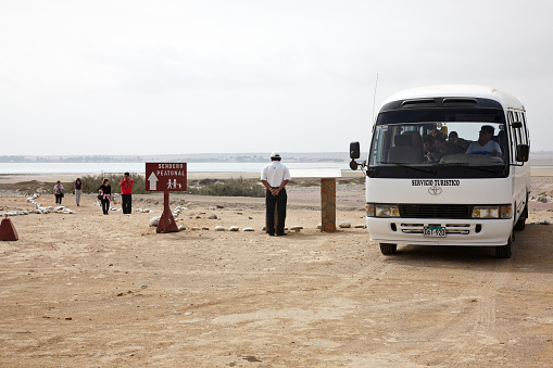 Paracas, Peru - May 23, 2013: White Peruvian tourist minibus with the driver inside with passengers making their way back onto the bus