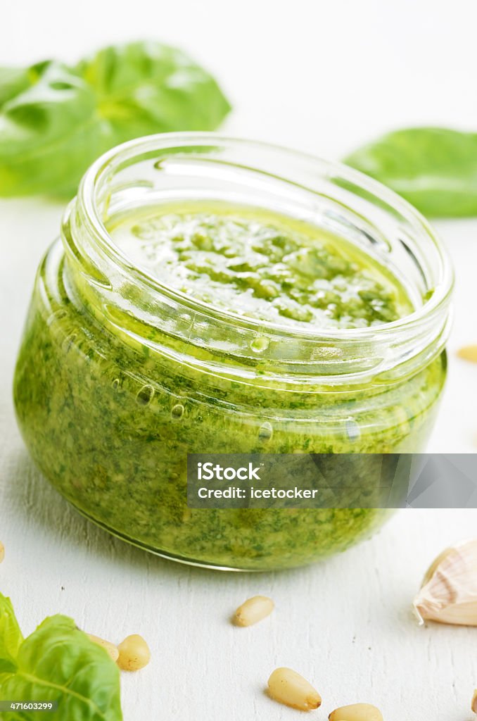 Pesto sauce jar Glass jar of pesto sauce on white kitchen table closeup Basil Stock Photo