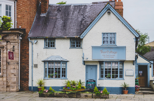 Henley in Arden, UK - June 16, 2013: Houses and shops along the pavement of the town of Henley-in-Arden, in the county of Warwickshire, the English Midlands, England, UK, Henley is a popular market town close to Stratford-upon-Avon and the high street is full of old buildings. It is a Sunday afternoon in summer, June and the weather is overcast. This is a Thai restaurant. 