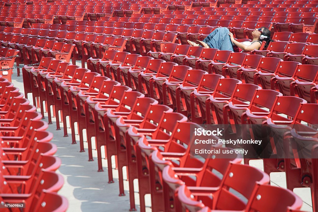 Kobieta słuchania słuchawki umieszczony pomiędzy czerwony pusty Stadion miejsc - Zbiór zdjęć royalty-free (Architektura)