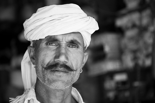 Bundi, India, December 3, 2012: Close view of an indian man with a mustache, wearing a white turban and shirt, who is looking to the camera on the street