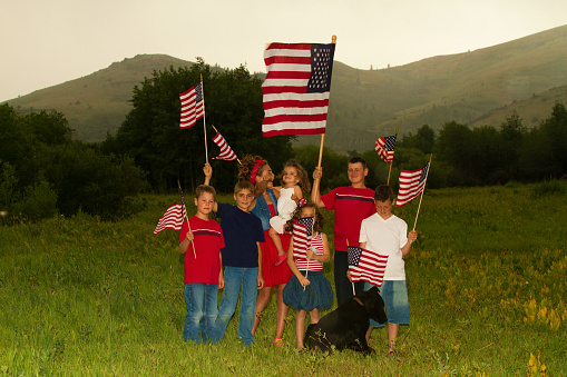 Kids playing with American flags on the 4th of July in a meadow. 