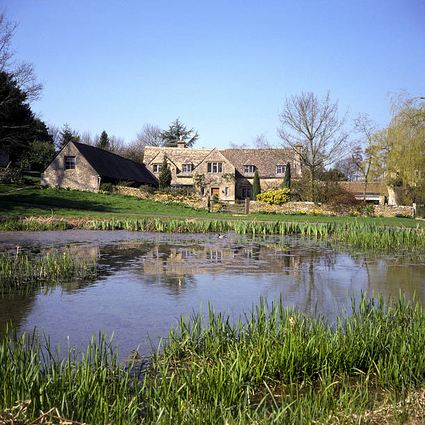 England, Oxfordshire, Cotswolds, Westwell, spring sunshine on homes around the village pond