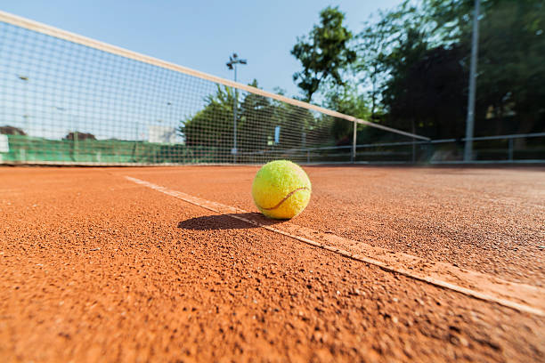 Wide angle close-up photograph of tennis ball on clay court.