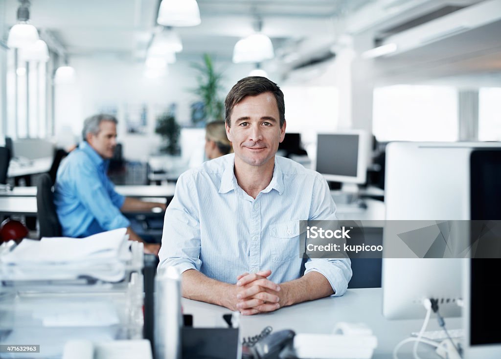 Comfortable in his work environment Composed businessman sitting at his desk with his coworkers in the background 30-39 Years Stock Photo