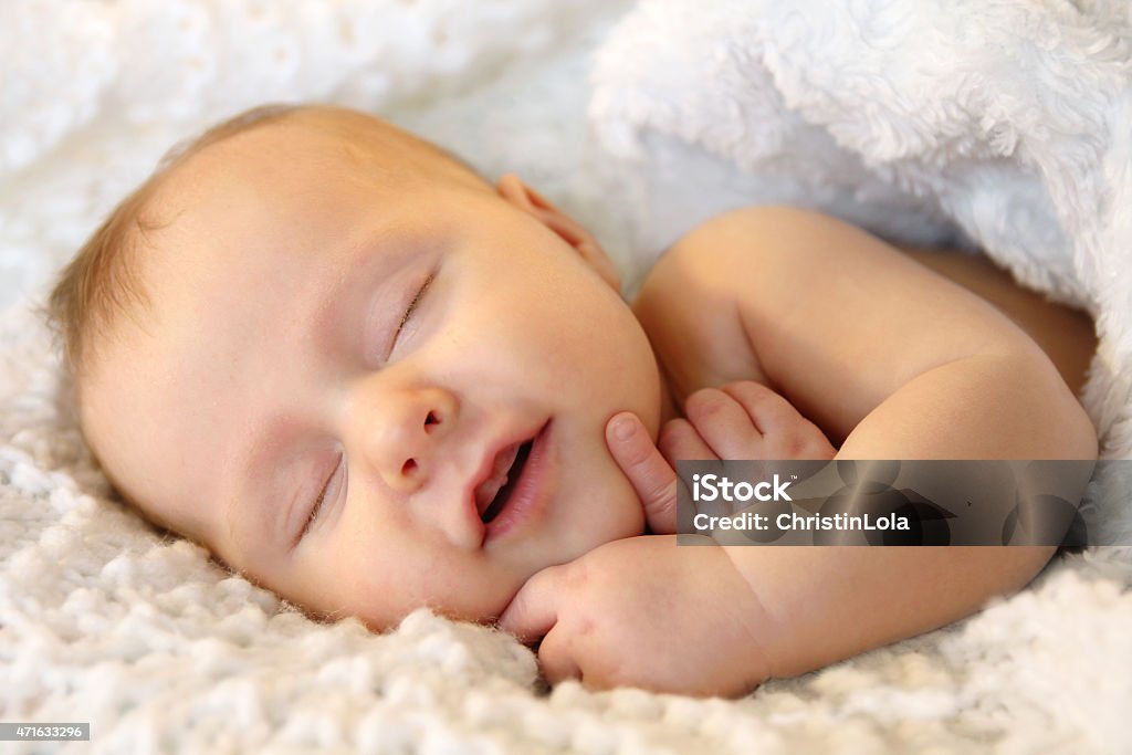 Smiling Sleeping Newborn Baby Girl Wrapped in White Blanket A cute one month old newborn baby girl is smiling in her sleep as she is cuddled up in a warm white blanket at naptime. Baby - Human Age Stock Photo