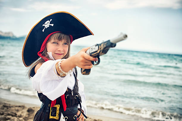 Brave little pirate girl on the beach aiming her pistol.