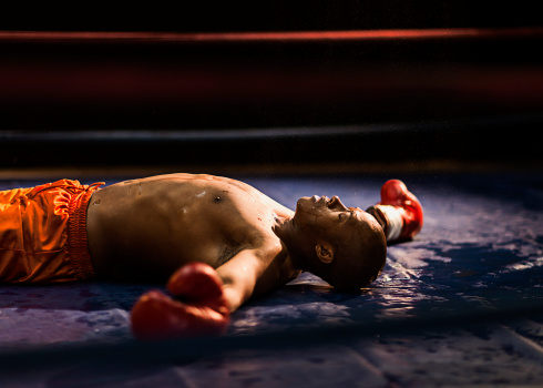 Boxer knocked out laying on the mat with his arms stretched out.
