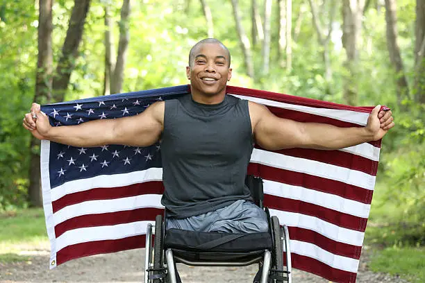 African american man sitting in wheelchair and holding out a flag at the park