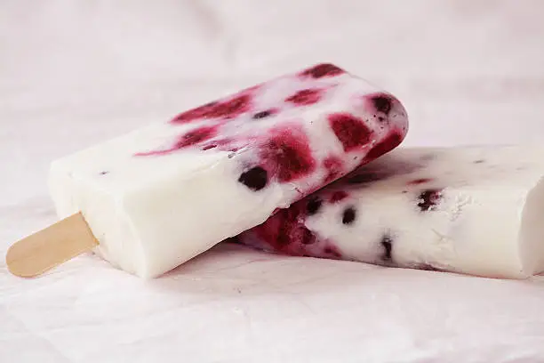 Coconut-based popsicle with frozen berries on a light-pink surface.