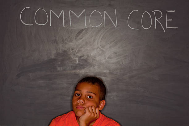 Elementary age boy in front of chalkboard with "common core" stock photo