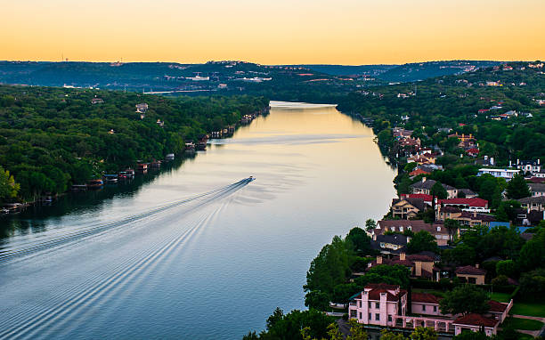 Sunrise Mount Bonnell Austin Texas Boat Ride Colorado River Sunrise Mount Bonnell Austin Texas Boat Ride Colorado River , with all the mansions and some of the most expensive houses in all of central texas. Houses in a community spread out across the edge of the river or town lake. One boat rides across the glass smooth lake making ripples and a wake in its path. As the sunrises over the hills the sky is lit up gold from golden hour. west lake stock pictures, royalty-free photos & images